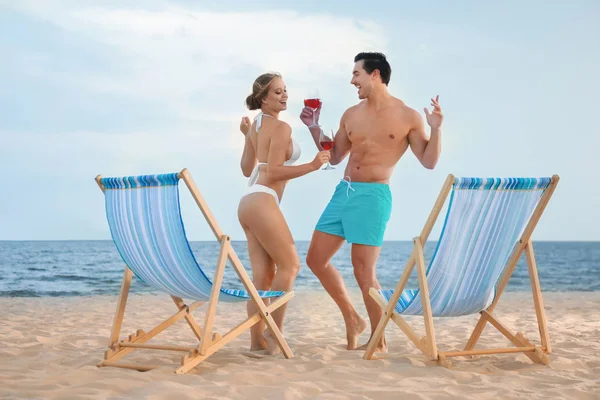 Feliz jovem casal dançando perto de espreguiçadeiras na praia do mar — Fotografia de Stock