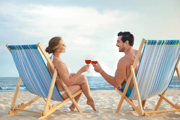 Heureux jeune couple avec des verres de vin assis sur des chaises longues à la plage de la mer — Photo