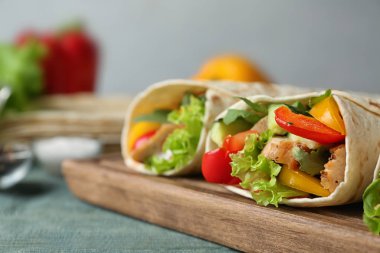 Gri arka plan karşı mavi ahşap masa üzerinde lezzetli et tortilla sarar ile Kurulu, closeup