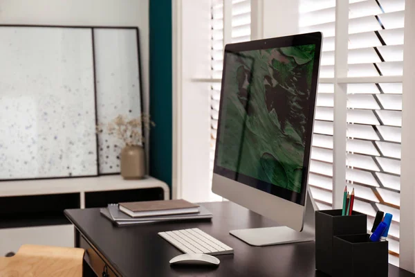 Bekväm arbetsplats nära fönster med vita horisontella persienner i rummet — Stockfoto