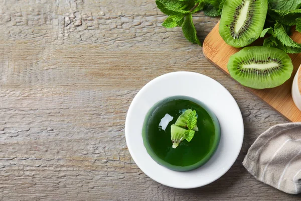 Delicious fresh green jelly with kiwi slices and mint on wooden table, flat lay. Space for text
