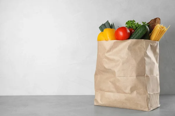 Paper bag with fresh vegetables on grey table against light background, space for text