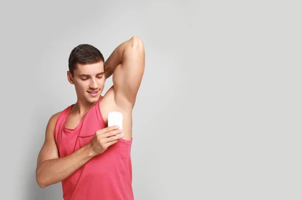 Young man applying deodorant to armpit on light background. Space for text — Stock Photo, Image