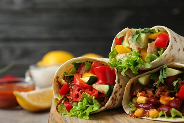 Bordo con deliziosi involucri tortilla di carne su tavolo leggero su sfondo nero, primo piano — Foto Stock