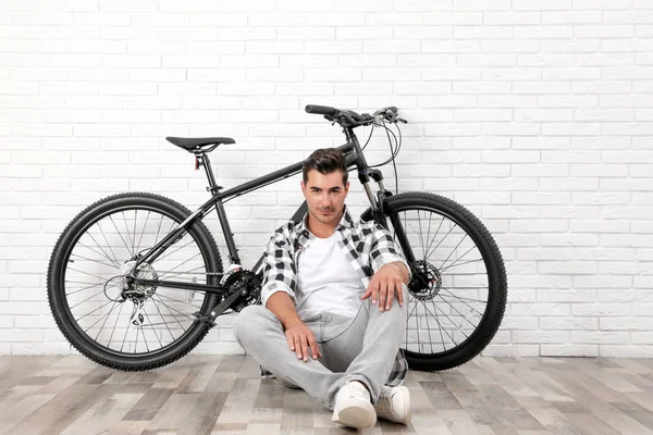 Красивий молодий чоловік з сучасним велосипедом біля білої цегляної стіни в приміщенні — стокове фото