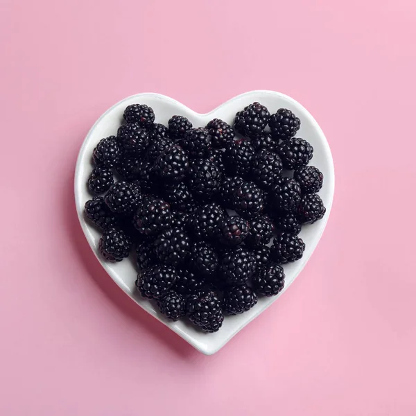 Placa em forma de coração de amoras maduras no fundo rosa, vista superior — Fotografia de Stock