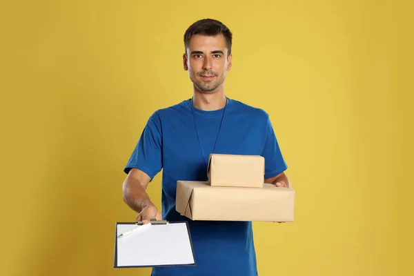 Happy young courier with parcels and clipboard on yellow background — Stok Foto