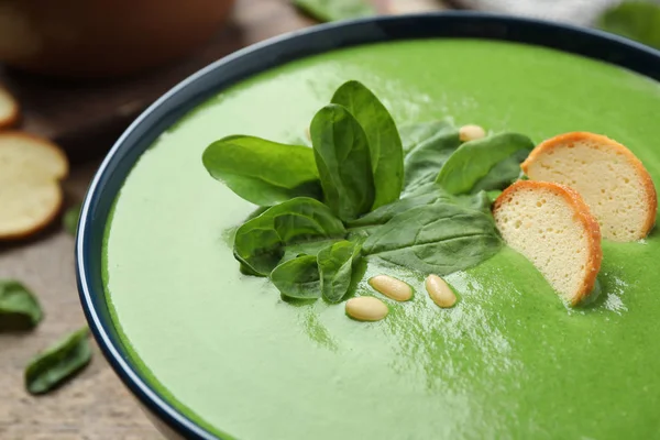 Bowl of healthy green soup with fresh spinach on wooden table, closeup view