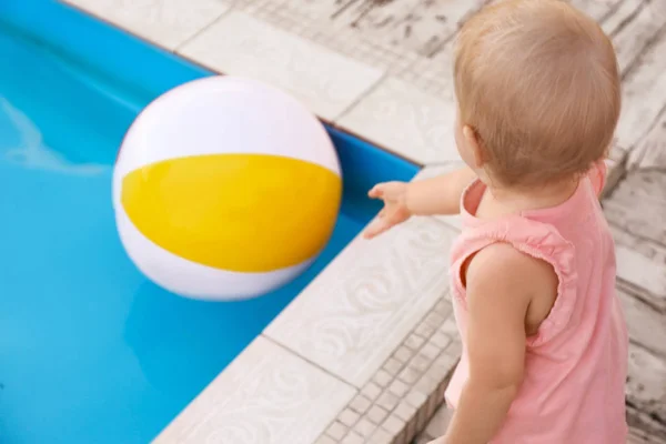 Little baby reaching for inflatable ball at outdoor swimming pool. Dangerous situation