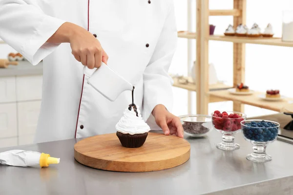 Жіночий шеф-кухар, що наливає шоколадний соус на кекс за столом на кухні, крупним планом — стокове фото