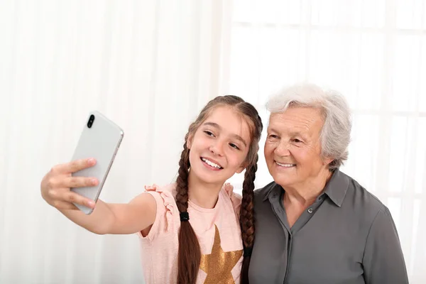 Счастливая симпатичная девочка делает селфи с бабушкой дома — стоковое фото