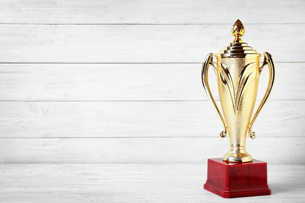 Golden trophy cup on white wooden background. Space for text