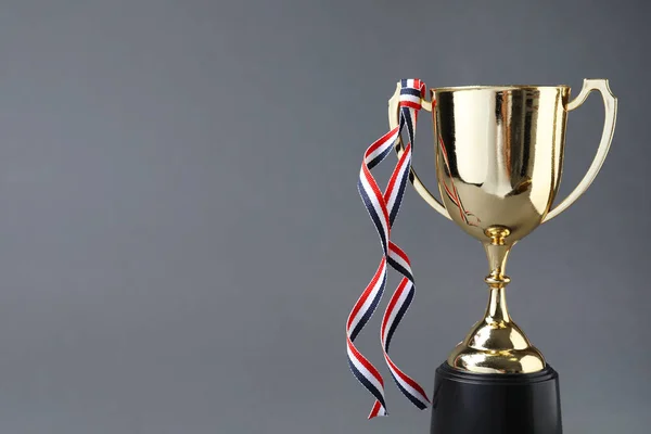 Gouden trofee beker met lint op grijze achtergrond. Ruimte voor tekst — Stockfoto