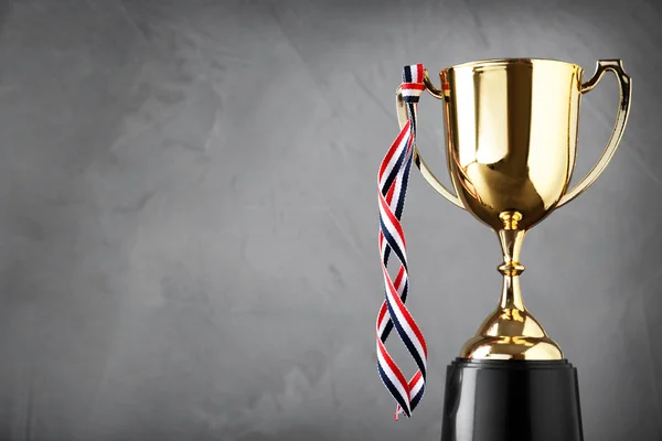 Golden trophy cup with ribbon on grey background. Space for text — Stock Photo, Image