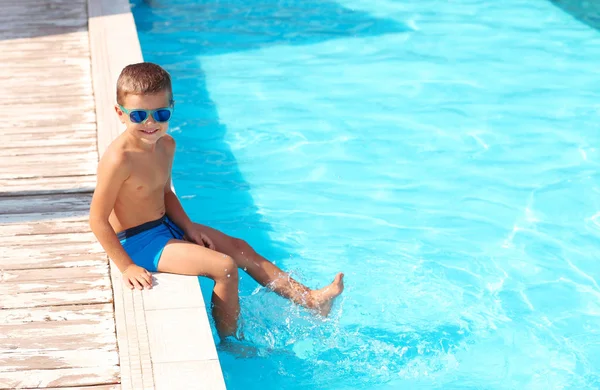 Lindo niño en gafas de sol sentado cerca de la piscina — Foto de Stock