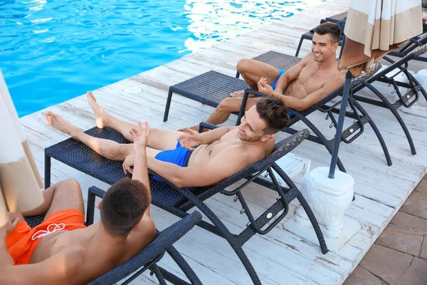 Felices jóvenes amigos relajándose en tumbonas cerca de la piscina — Foto de Stock