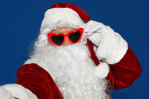 Настоящий Санта-Клаус в солнечных очках делает селфи на синем фоне — стоковое фото