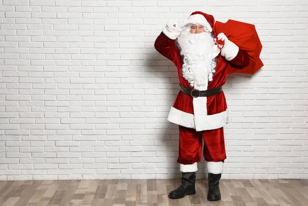 Auténtico Santa Claus con bolsa llena de regalos contra la pared de ladrillo blanco. Espacio para texto —  Fotos de Stock