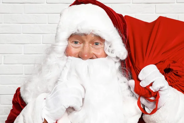 Papai Noel autêntico com saco cheio de presentes contra parede de tijolo branco — Fotografia de Stock