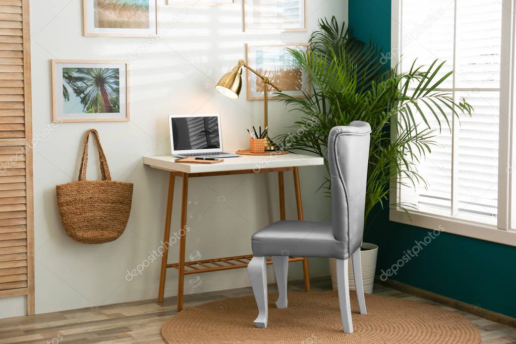 Stylish home workplace with elegant grey chair near window. Interior design