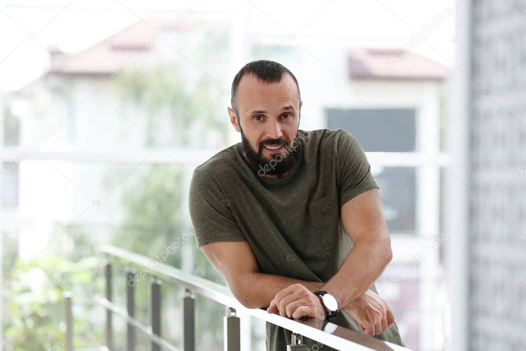 Portrait of handsome mature man leaning on handrail indoors