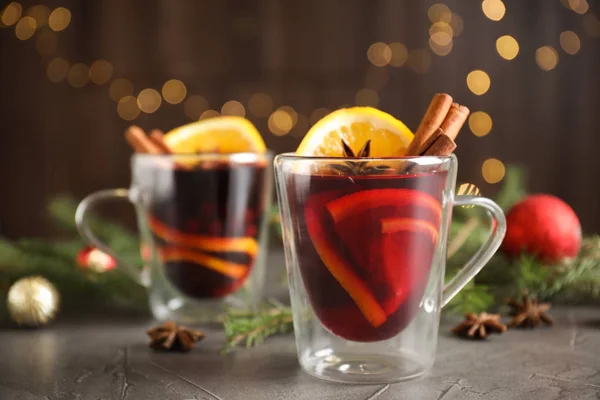 Glasbecher mit Glühwein auf grauem Tisch gegen festliches Licht — Stockfoto