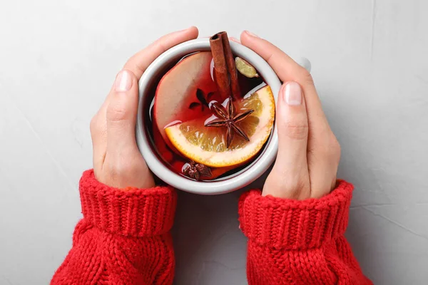 Mujer sosteniendo taza de sabroso vino caliente en la mesa gris, vista superior — Foto de Stock