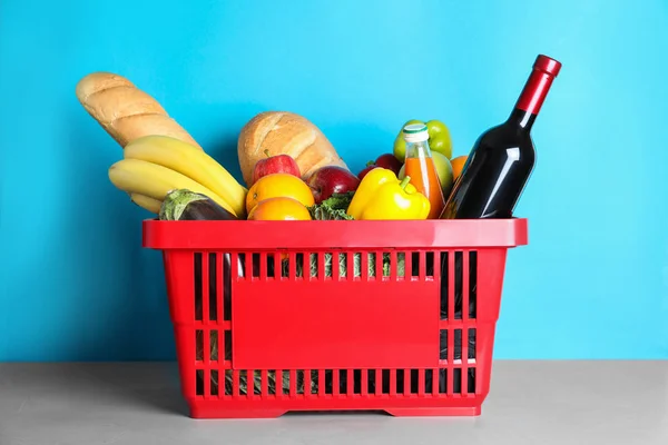 Cesta de la compra con productos de alimentación sobre mesa gris sobre fondo azul claro — Foto de Stock