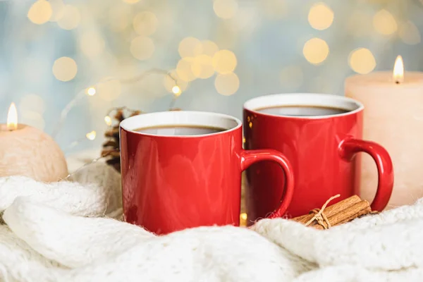 Cups of hot winter drink and burning candles on knitted plaid against blurred lights — Stock Photo, Image