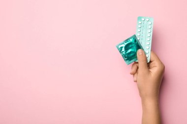 Pembe arka planda prezervatif ve doğum kontrol hapları tutan kadın, metin için alan ile üst görünümü. Güvenli seks