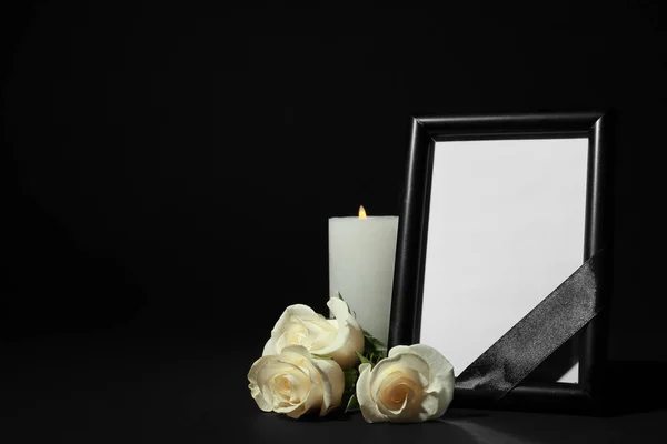 Moldura de fotos funerárias com fita, rosas brancas e vela na mesa escura contra fundo preto. Espaço para design — Fotografia de Stock