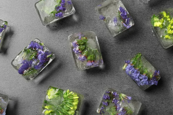 Cubes de glace avec des fleurs sur fond de pierre grise, plat — Photo