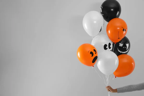 Donna che tiene palloncini di colore per la festa di Halloween su sfondo grigio chiaro, primo piano. Spazio per testo — Foto Stock