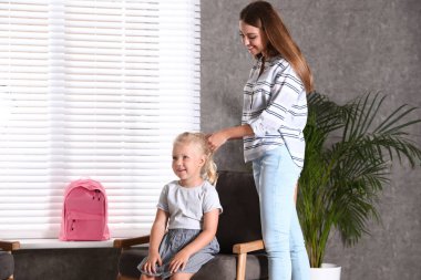 Mutlu genç anne evde küçük çocuğunun saçlarını örme. Okula hazırlanmak