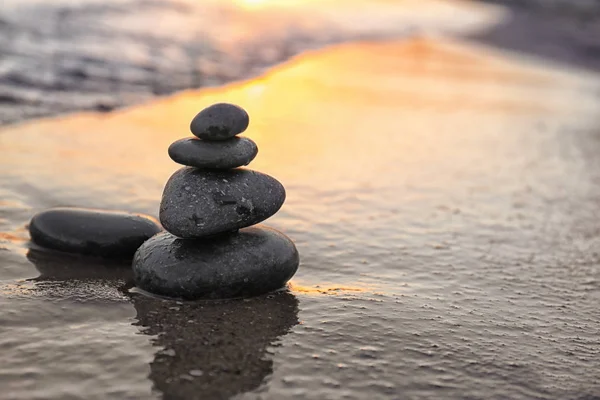 Ciemne kamienie na piasku w pobliżu morza o zachodzie słońca, miejsce na tekst. Koncepcja Zen — Zdjęcie stockowe