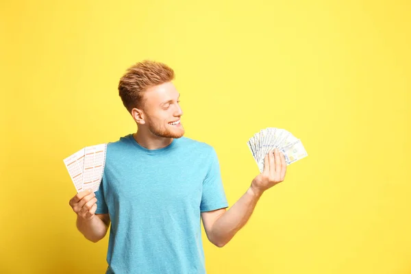 Muotokuva onnellinen nuori mies, jolla on rahaa ja arpoja keltaisella taustalla — kuvapankkivalokuva