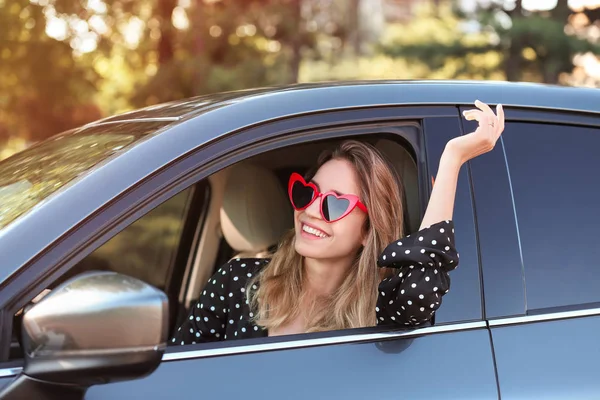 Jovem mulher bonita vestindo óculos em forma de coração no carro — Fotografia de Stock