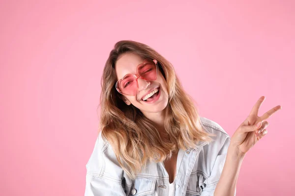 Jovem mulher bonita vestindo óculos em forma de coração no fundo rosa — Fotografia de Stock