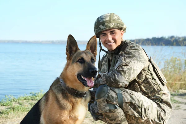 Hombre en uniforme militar con perro pastor alemán cerca del río — Foto de Stock
