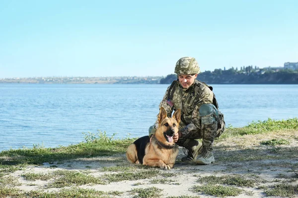 Hombre en uniforme militar con perro pastor alemán cerca del río, espacio para el texto — Foto de Stock