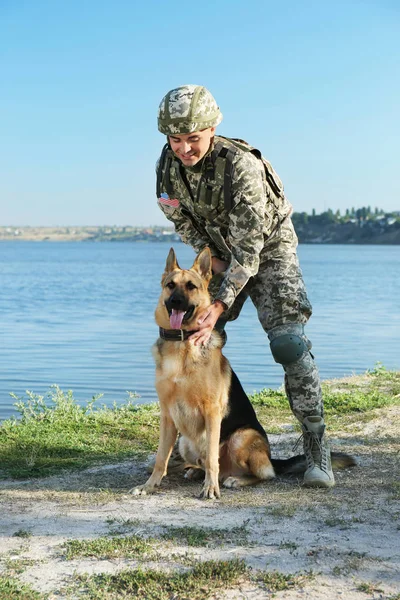 Muž ve vojenské uniformě s německý ovčák poblíž řeky — Stock fotografie