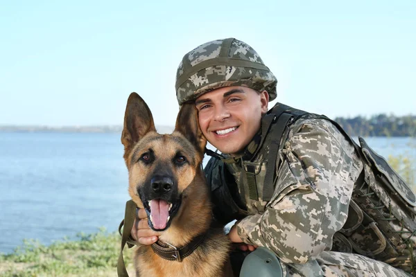 Hombre en uniforme militar con perro pastor alemán cerca del río — Foto de Stock