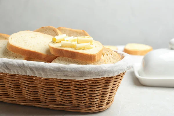 軽い大理石のテーブルの上にウィッカーバスケットにバターとおいしい新鮮なパンのスライス — ストック写真