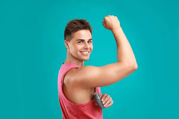 Giovane uomo che applica il deodorante all'ascella su sfondo blu — Foto Stock