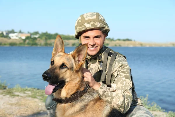 Hombre en uniforme militar con perro pastor alemán cerca del río — Foto de Stock