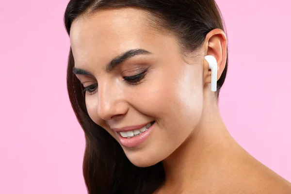 ピンクの背景にワイヤレスイヤホンを通じて音楽を聴く幸せな若い女性、クローズアップ — ストック写真
