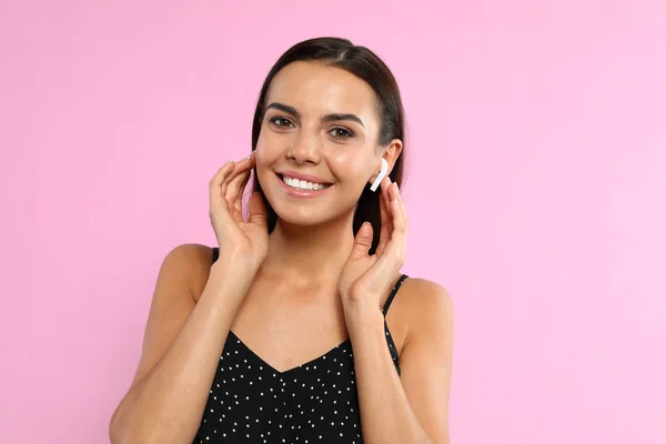 Mujer joven y feliz escuchando música a través de auriculares inalámbricos sobre fondo rosa — Foto de Stock