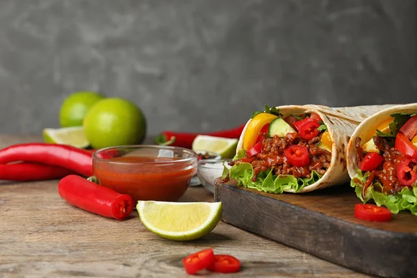 Gri arka plan karşı ahşap masa üzerinde lezzetli et tortilla sarar ile Kurulu — Stok fotoğraf