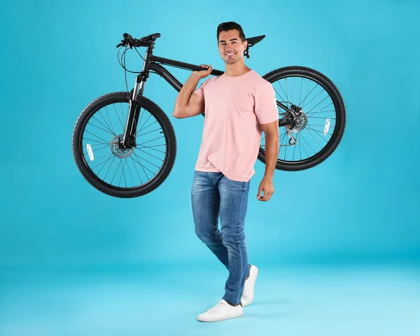 Красивий молодий чоловік з сучасним велосипедом на світло-блакитному тлі — стокове фото