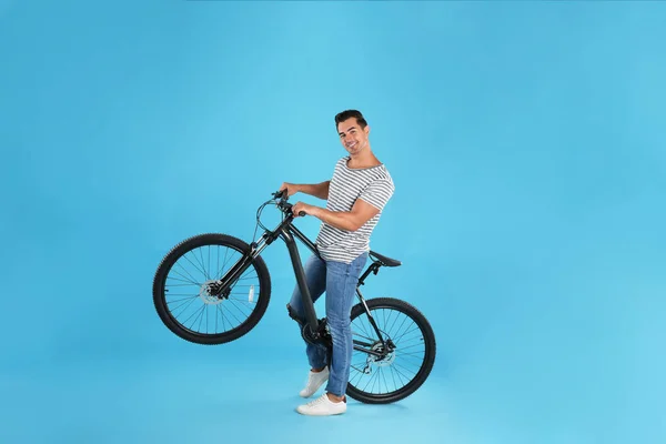 Schöner junger Mann mit modernem Fahrrad auf hellblauem Hintergrund — Stockfoto